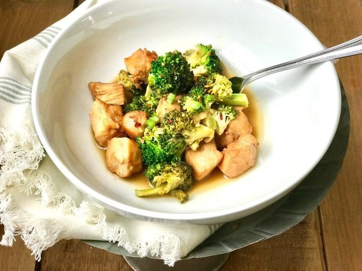 a white bowl filled with broccoli and chicken on top of a wooden table