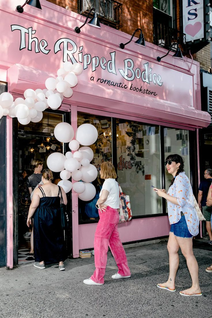 people are walking in front of the ripped bodie store with white balloons hanging from it's windows