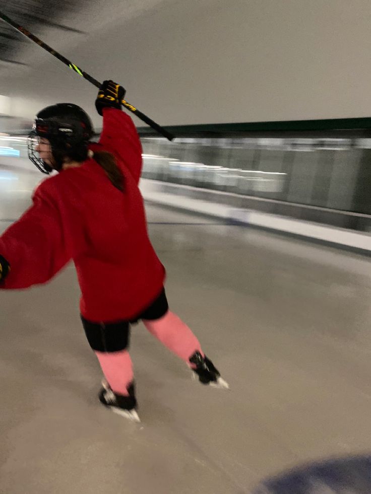 a woman in red jacket and black shorts skating on an indoor ice rink with poles