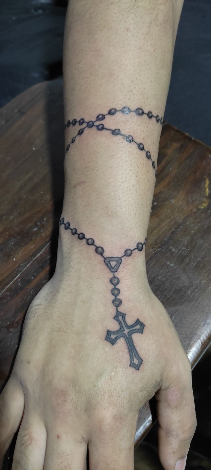 a man with a rosary tattoo on his wrist and hand is holding the cross that he has placed in front of him