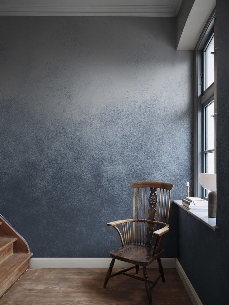 a chair sitting in front of a window next to a wooden stair case with a painting on the wall