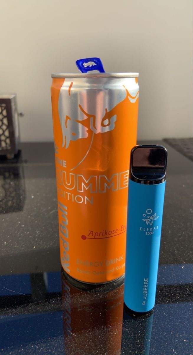 an orange and blue cup sitting on top of a table next to a can of soda