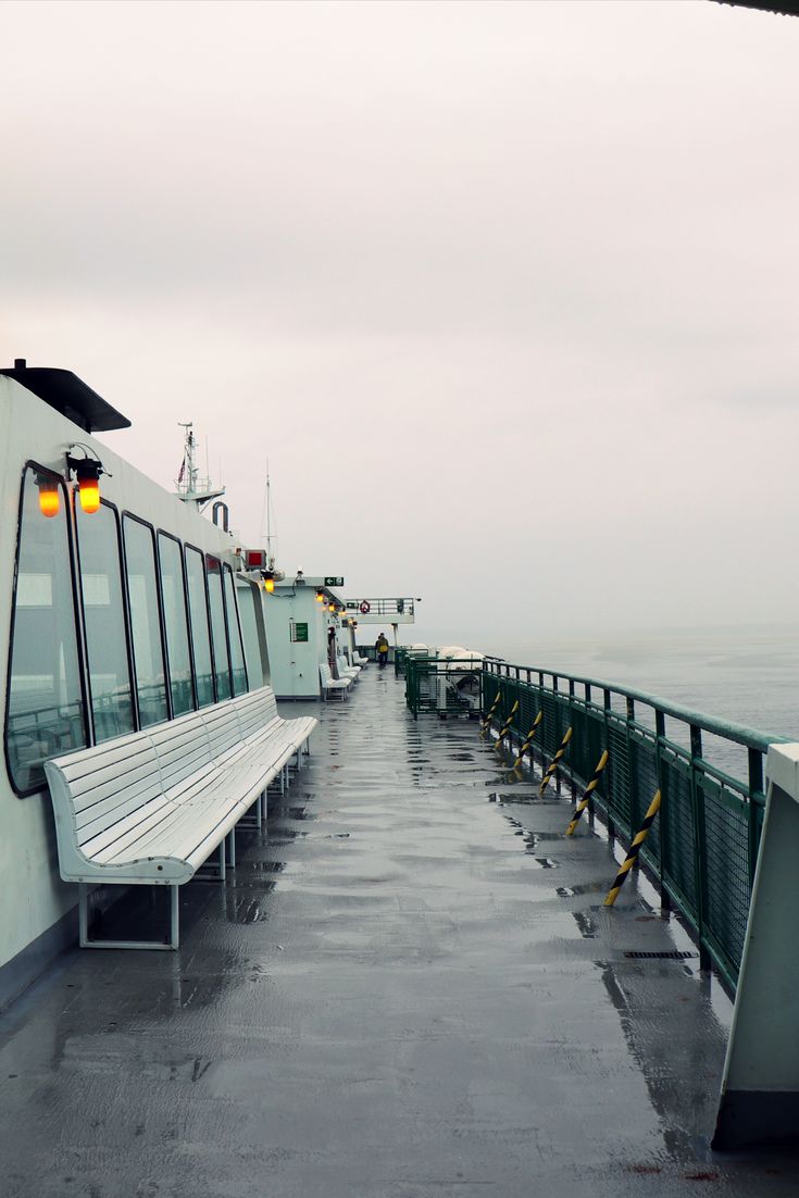 a long white bench sitting on top of a pier next to the ocean in the rain