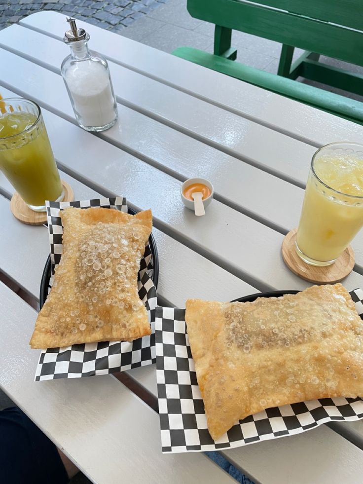 two pastries sitting on top of black and white checkered plates next to drinks