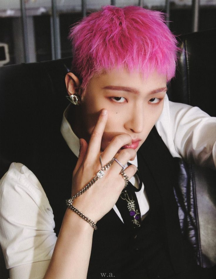 a person with pink hair sitting in a chair and holding their hand to his face