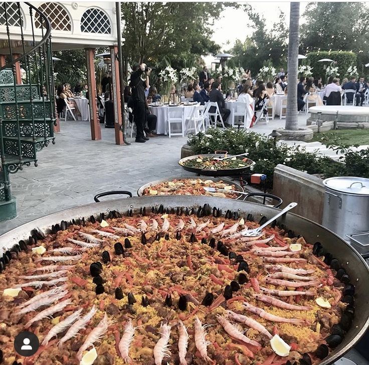 a large pan filled with lots of food on top of a metal tray next to tables