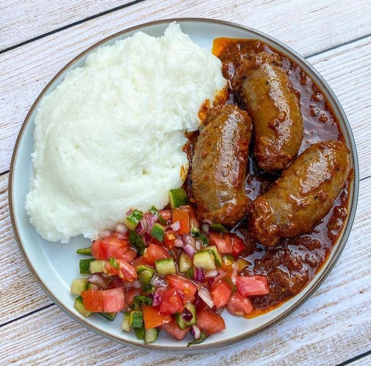 a white plate topped with meat and vegetables next to mashed potatoes on top of a wooden table