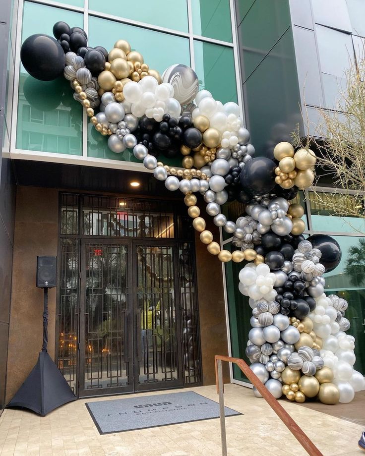 an entrance to a building decorated with black, white and gold balloons