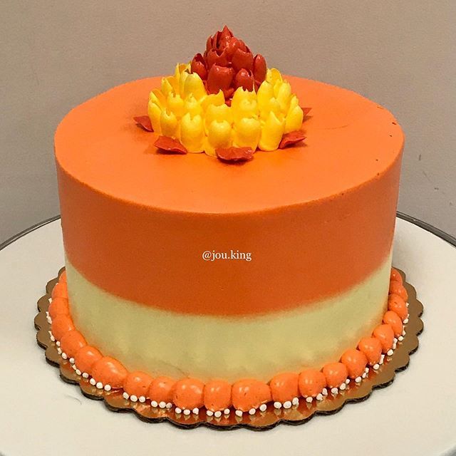 an orange and yellow cake with flowers on top is sitting on a white platter