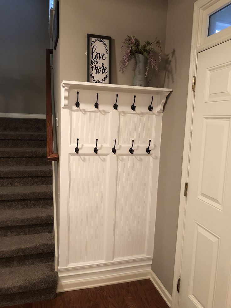 a white coat rack with hooks on it and some stairs in the back ground behind it