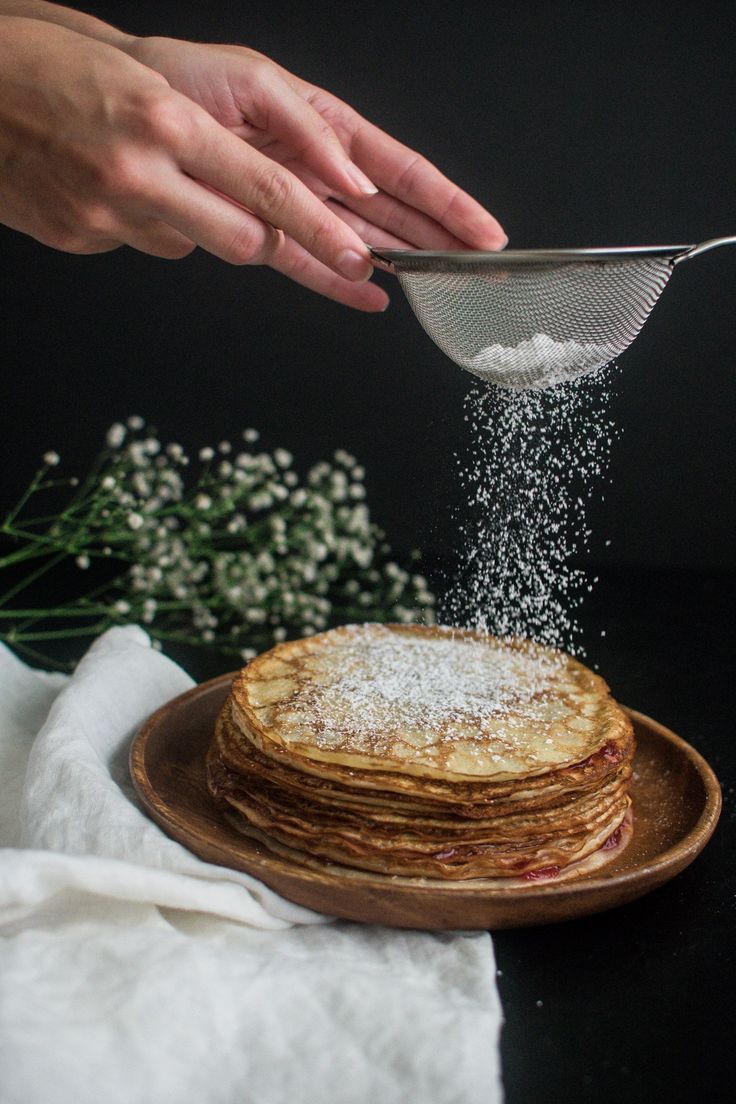 a stack of pancakes being sprinkled with powdered sugar on a wooden plate