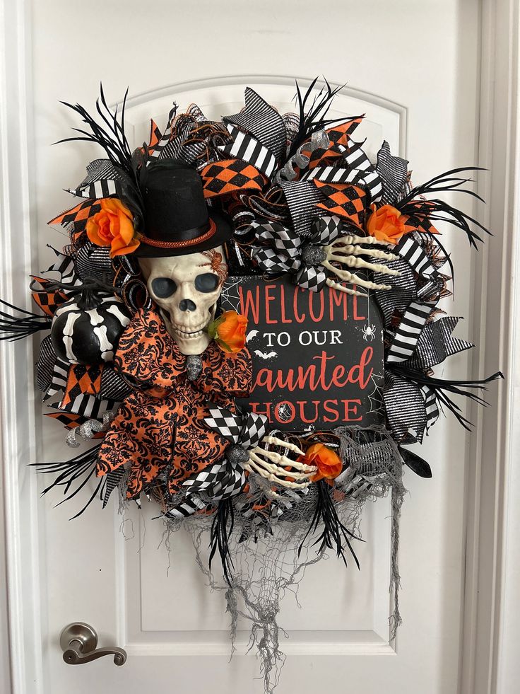 a halloween wreath decorated with black and orange decorations, skeleton hands and a top hat that says welcome to our haunted house