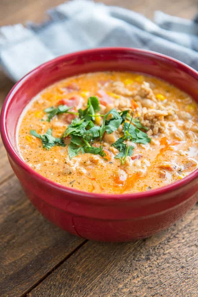 a red bowl filled with soup sitting on top of a wooden table next to a napkin