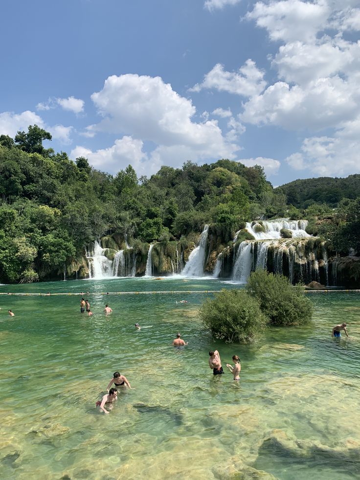 many people are swimming in the water near a waterfall and some trees with green leaves