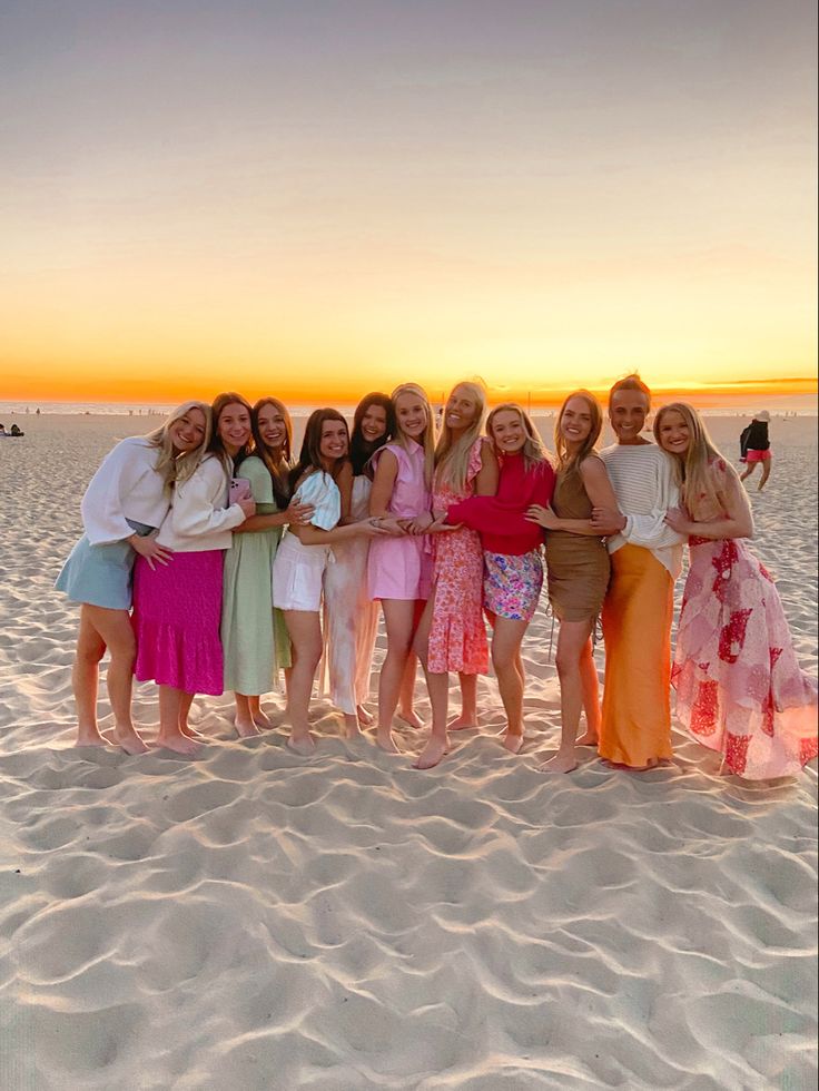 a group of women standing next to each other on top of a sandy beach at sunset