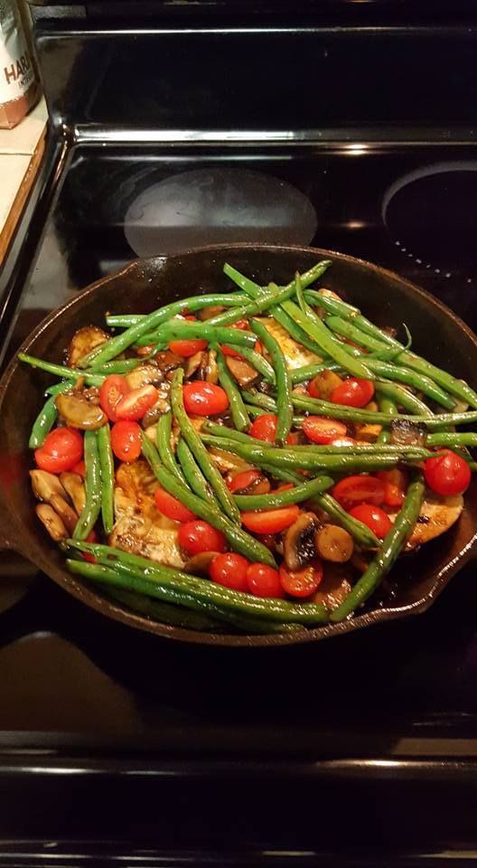 a pan filled with green beans and tomatoes on top of a stove next to an oven