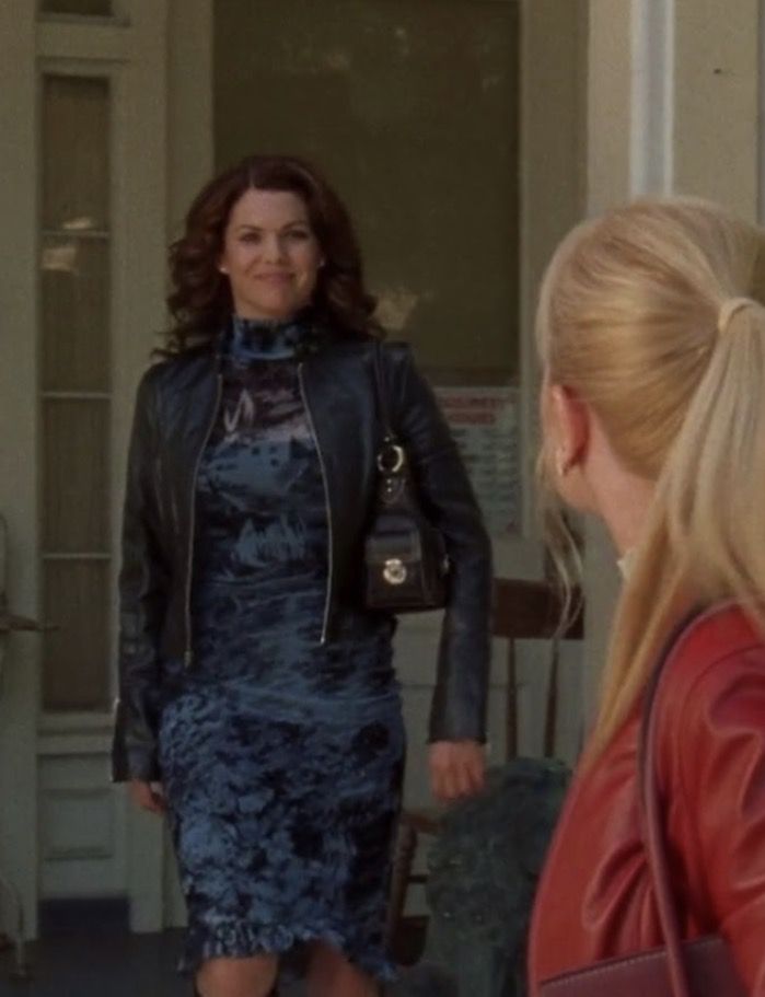 a woman in a blue dress and leather jacket is talking to another woman wearing a red coat