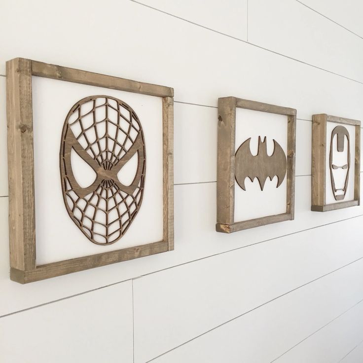 three wooden frames are hanging on the wall with various pictures in them, one has a spiderman mask and two have batman masks