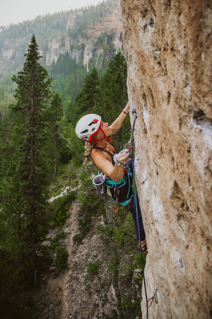 a woman climbing up the side of a mountain with her helmet on and hands in the air