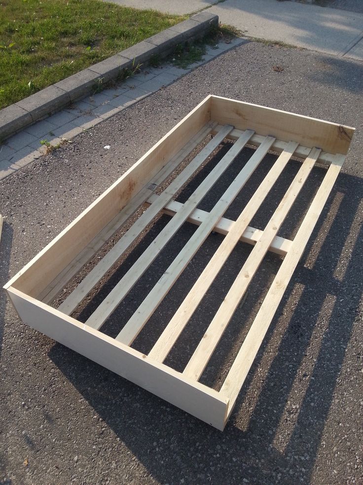 a wooden bed frame laying on the ground next to a sidewalk with grass in the background