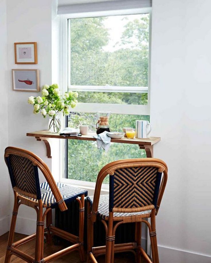 two chairs sitting at a table in front of a window with a vase on it