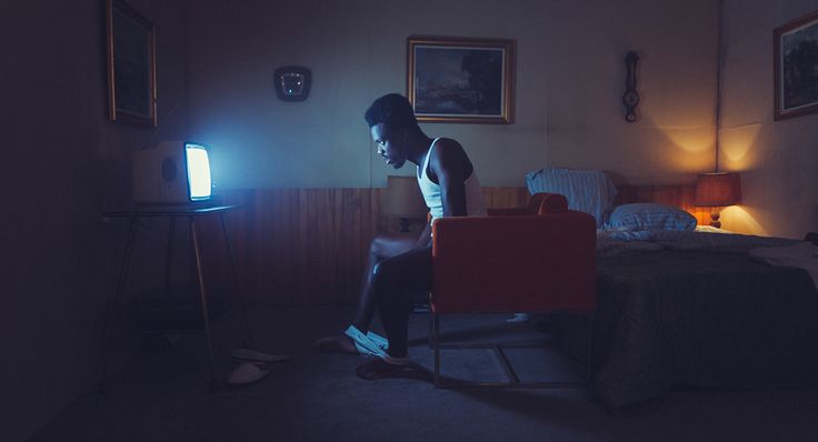 a man sitting on a chair in a dimly lit room with a television and bed