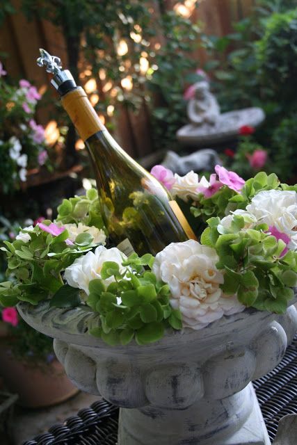 a vase with flowers and a bottle of wine sitting on a table in a garden