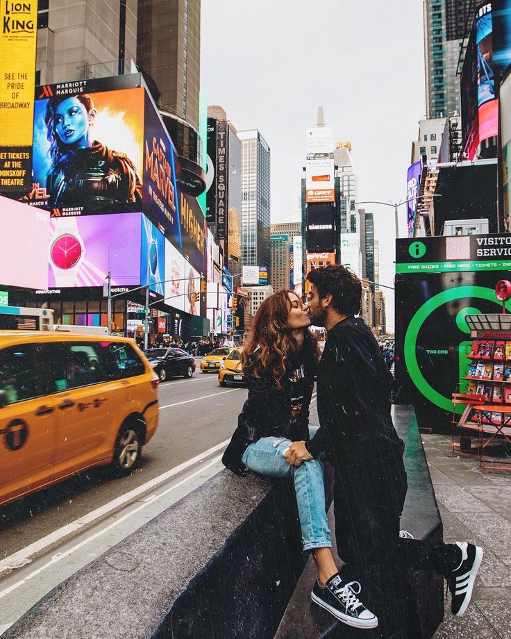 two people standing on the side of a road in new york city, one kissing the other