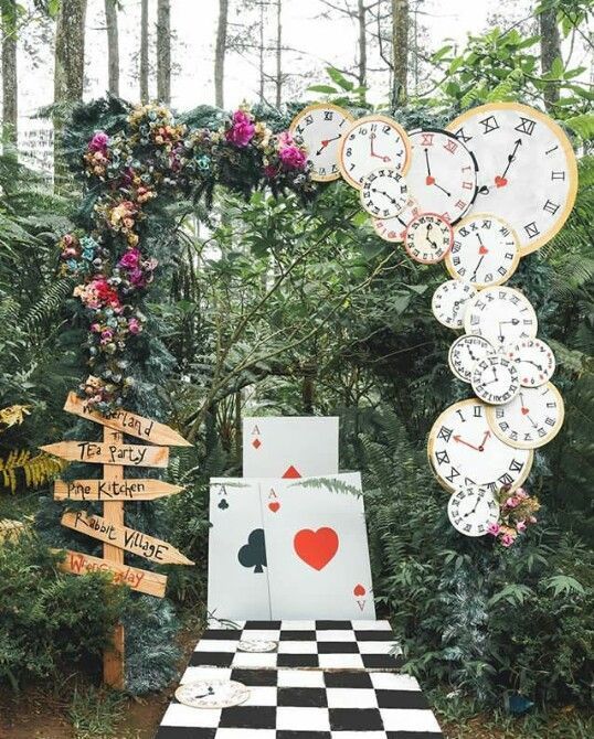 a checkerboard table topped with lots of clocks in the middle of a forest