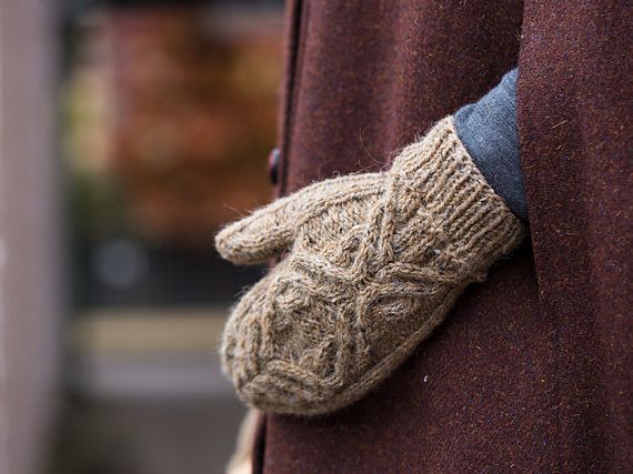 a pair of mittens hanging from the side of a coat on a person's arm