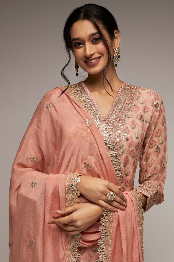 Editor's Note This pretty ensemble in this Nusrat floral jaal, combines gota and dori buttis with an intricate border embroidery. The short tunic with matching dupatta embroidered in sequins and gold thread, and voluminous sharara adds a feminine grace. Fabric: Dupatta: crepe, kurta: georgette, sharara: georgette Color: Pink Component: Sharara, kurta and dupatta Occasion: Festive Note: Product colour may slightly vary due to photographic lighting sources Care: Dry Clean Only About the Designer G Diwali Palazzo Set With Sheer Dupatta In Dola Silk, Diwali Dola Silk Palazzo Set With Sheer Dupatta, Pink Sharara With Straight Kurta For Transitional Seasons, Pink Dola Silk Palazzo Set With Dupatta, Pink Dola Silk Palazzo Set For Diwali, Pink Chinon Palazzo Set With Gota Work, Festive Pink Dola Silk Palazzo Set, Bollywood Dola Silk Palazzo Set With Chikankari Embroidery, Chikankari Embroidered Dola Silk Sharara For Reception