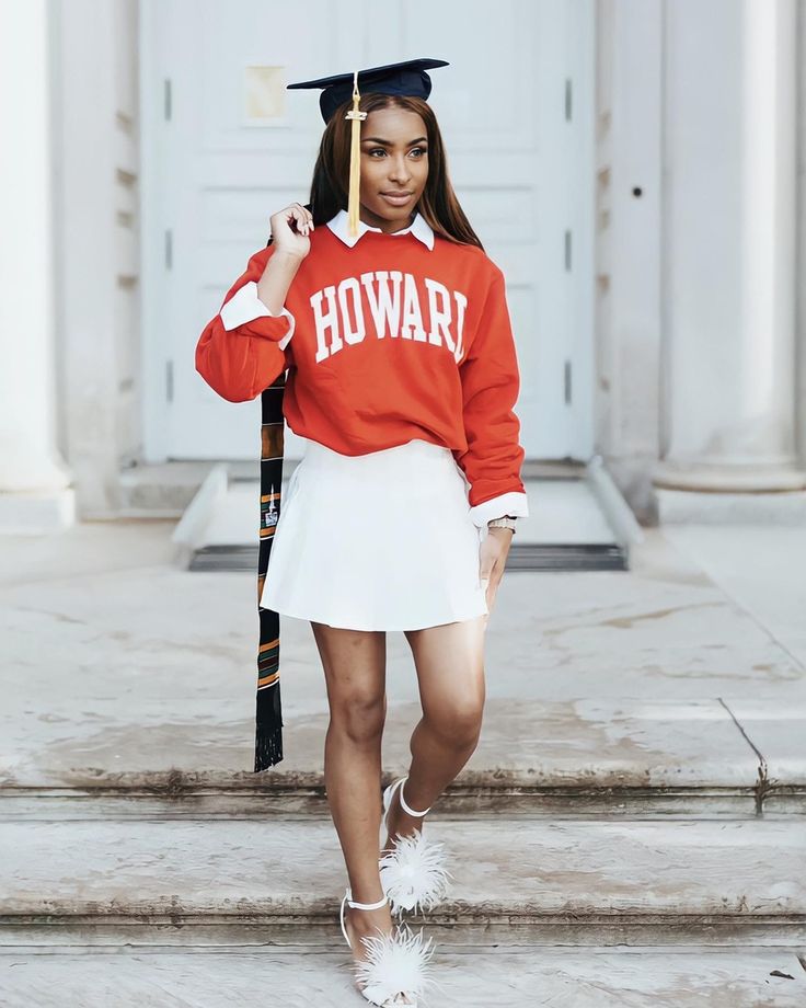 a woman in a red sweatshirt and white skirt is walking down the steps with her graduation cap on