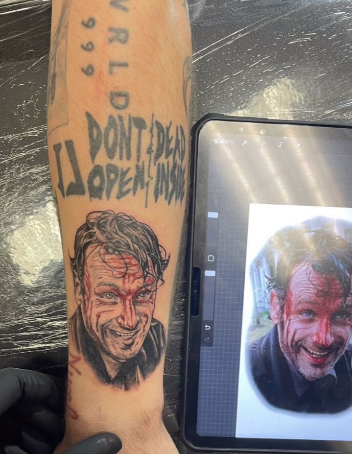 a man's arm with an image of the walking dead on it next to a cell phone