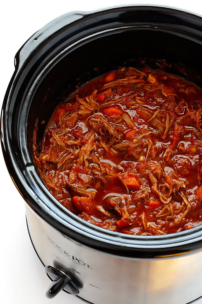 a crock pot filled with beef and carrots on top of a white table