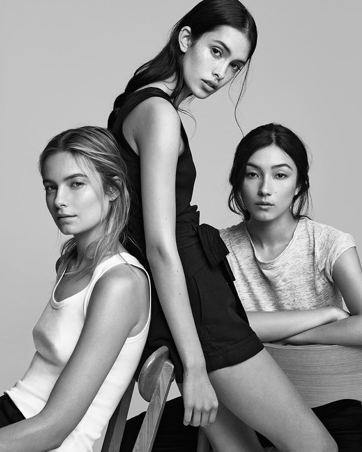 three young women sitting on top of a chair in front of a gray background,