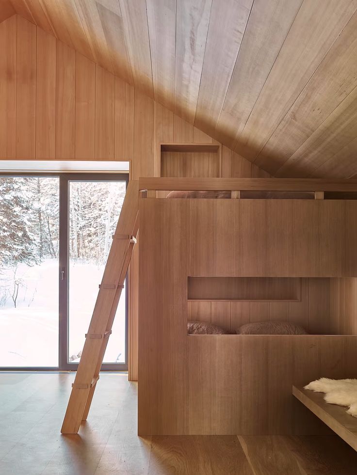 a bunk bed in the corner of a room with wooden walls and flooring that has snow on the ground