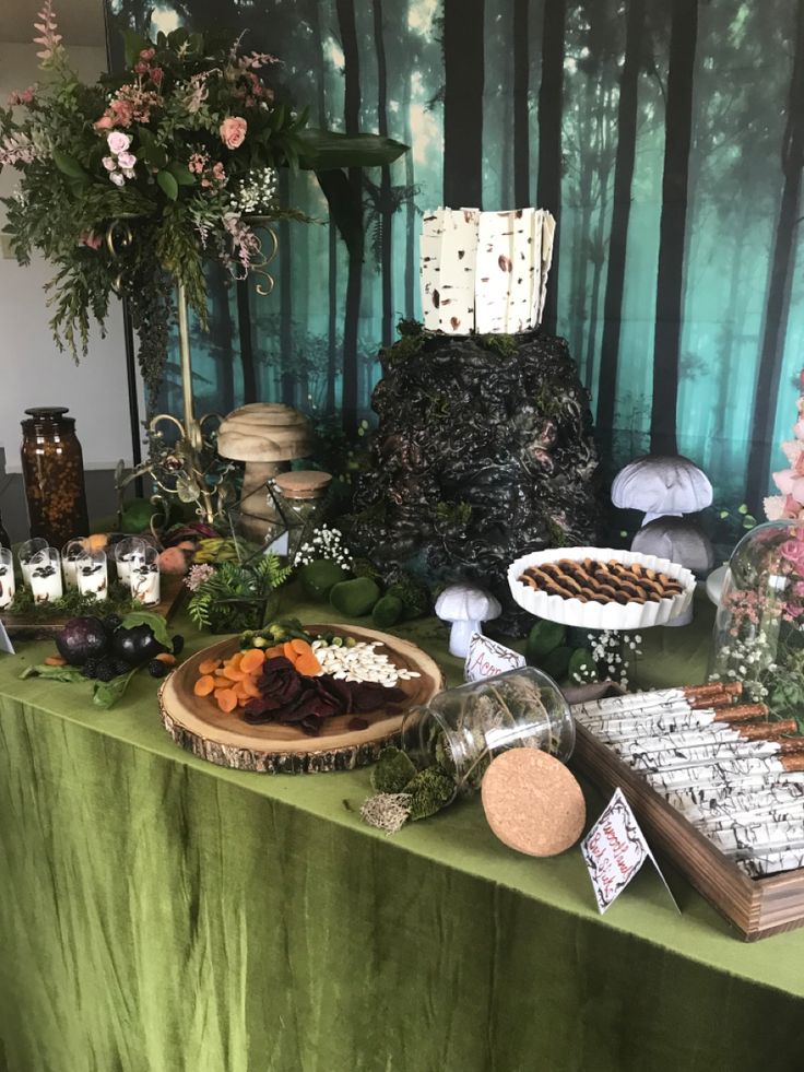 a table topped with lots of food and desserts next to a forest wallpaper