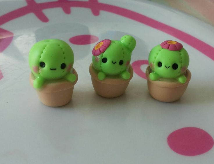 three little green toy animals sitting in small clay pots on a pink and white table