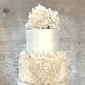 a three tiered white wedding cake with flowers on top, against a brick wall