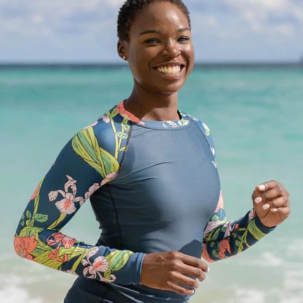 a woman standing on the beach in front of the ocean wearing a wet suit and smiling