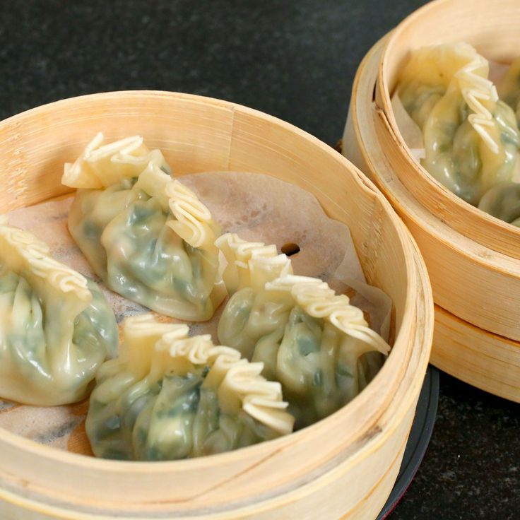 three wooden containers filled with dumplings on top of a black table next to each other