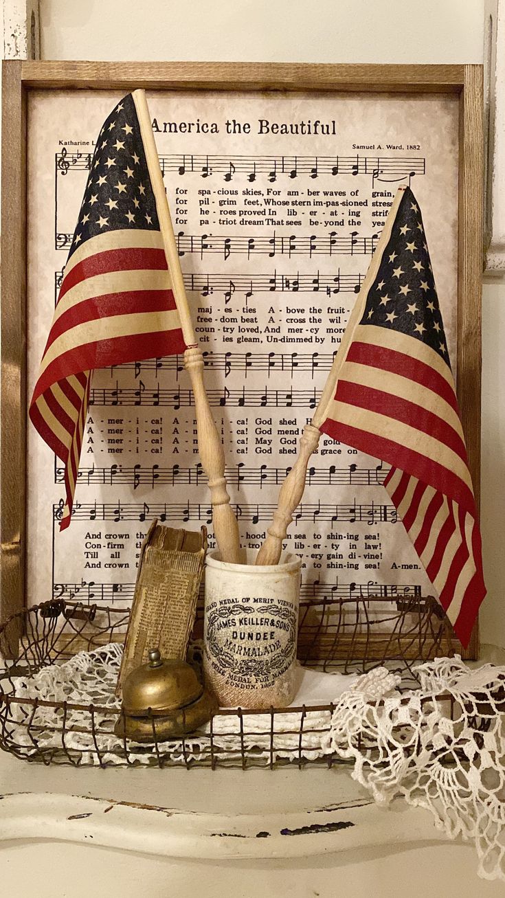 an american flag and two wooden flags on top of a shelf with music sheets in the background