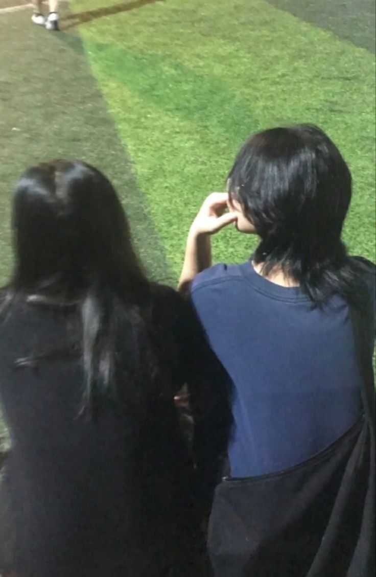 two women sitting on a bench watching a baseball game