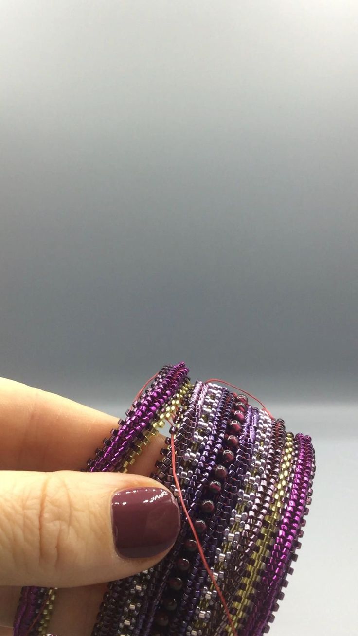 a woman's hand holding a stack of purple and gold beaded bracelets