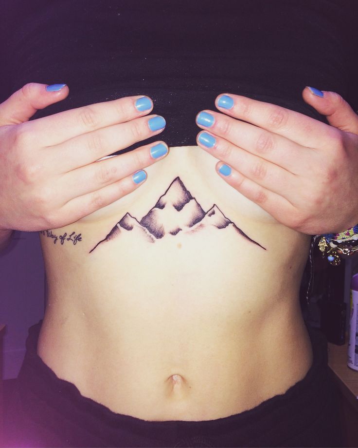 a woman's stomach with mountains tattooed on the side and her hands over her belly