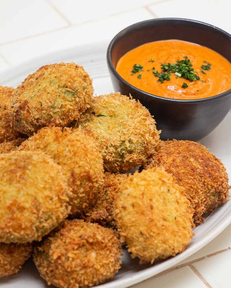 some fried food on a white plate next to a bowl of tomato soup and dipping sauce