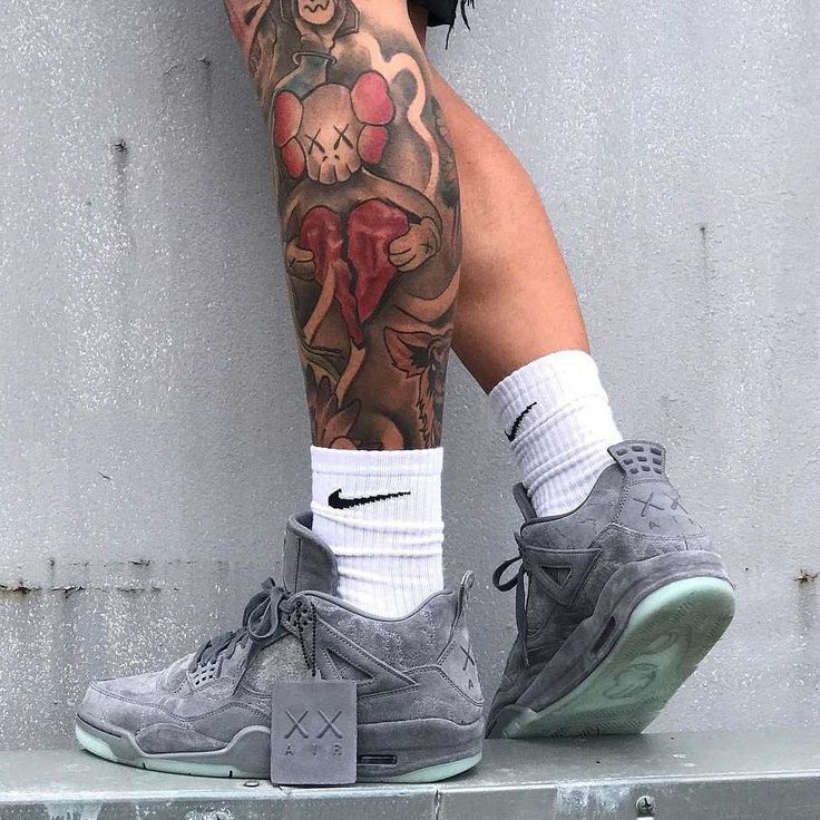 a person with tattoos on their legs wearing nike basketball shoes and socks, standing next to a wall