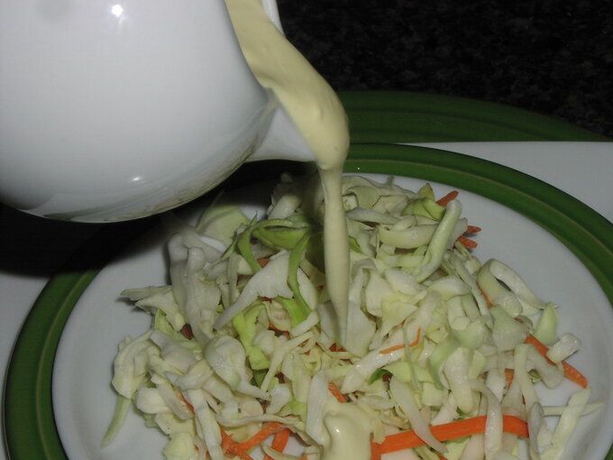 someone pouring dressing onto a plate of coleslaw