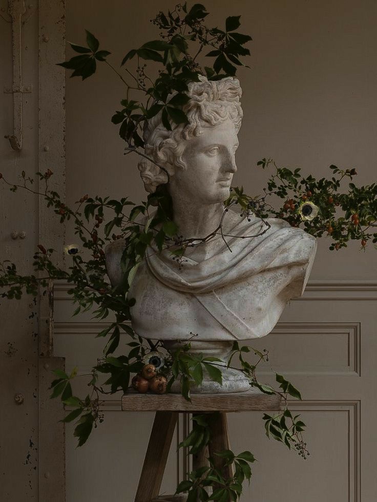 a statue with flowers in it's hair on top of a wooden stand next to a wall