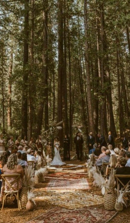 an outdoor ceremony in the woods with lots of people sitting on chairs and looking at each other